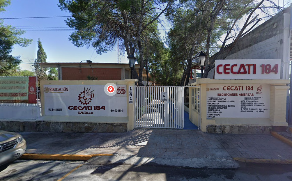 Fotografía en la que se muestra la entrada del plantel, conformada por dos muros de color blanco con borde amarillo, debajo del borde en letras rojas dice CECATI 184. En medio de los muros hay una reja de color blanco que da acceso a las instalaciones.